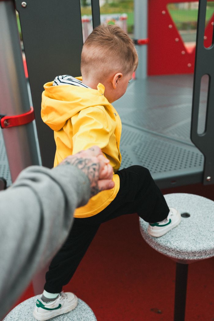 my-qualifications A child in a yellow hoodie climbs play equipment with parental guidance.
