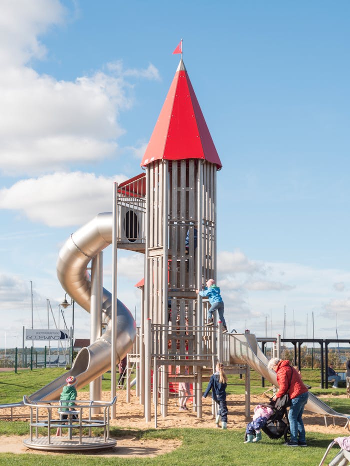 service-02 Kids enjoy playing on a large playground structure with slides and a climbing tower on a sunny day.
