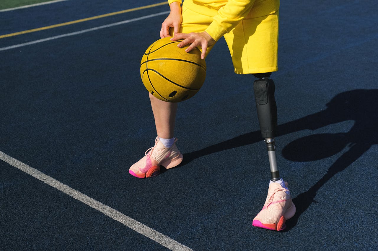 about-me Close-up of an adaptive athlete with a prosthetic leg holding a basketball on a sports court.
