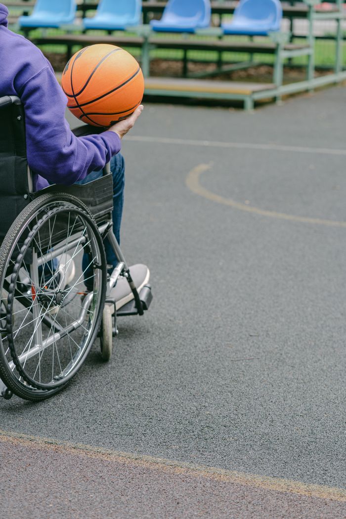 hero-img A person in a wheelchair holding a basketball on an outdoor court, promoting inclusivity in sports.